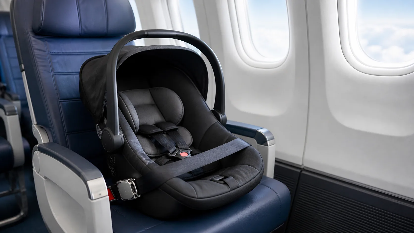 Babyautostol spændt fast med flysele på et passagersæde i en flykabine ved vinduet